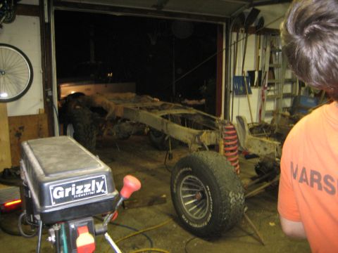 1990 Ford Bronco - A bare truck chassis sits in a garage, possibly for parts or repair, with a drill press in the foreground.