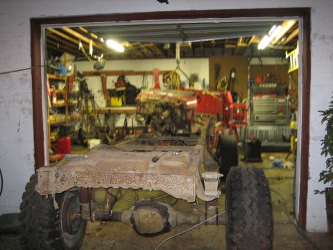 1990 Ford Bronco - Truck chassis sits in a garage with tools and equipment in the background.