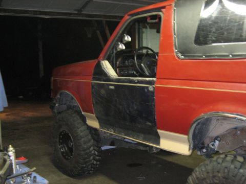1990 Ford Bronco - The 1990 Ford Bronco shows its distinctive half-door configuration and red paint with tan accents.