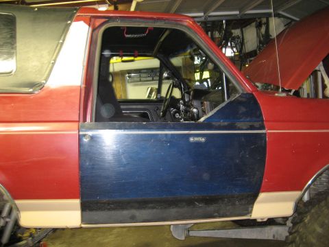 1990 Ford Bronco - The interior of a red and blue SUV is visible, with the hood open revealing the engine bay.