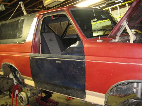 1990 Ford Bronco - The vehicle is on jack stands with the doors removed and the hood open, indicating it is undergoing maintenance or repair.