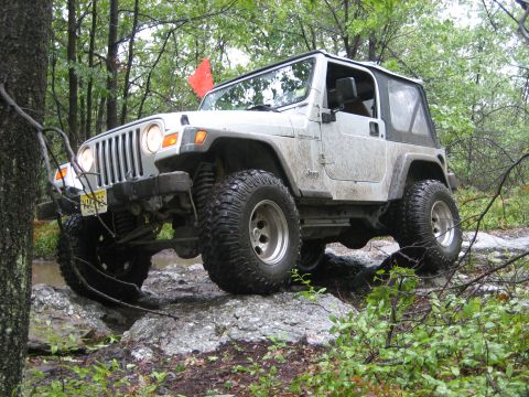 1990 Ford Bronco - A white Jeep Wrangler navigates a rocky trail in a wooded area.