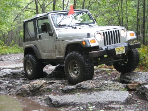 1990 Ford Bronco - Silver Jeep Wrangler TJ tackling a rocky trail with a soft top.