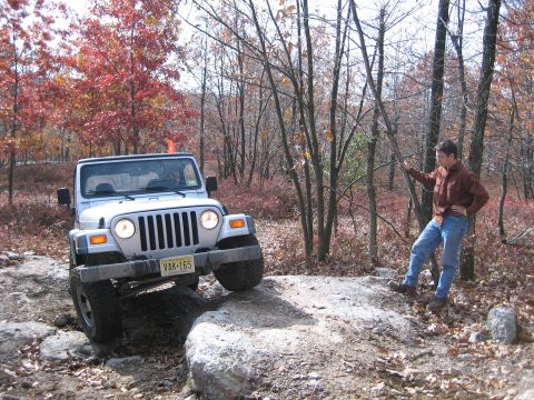 1990 Ford Bronco - A man watches a Jeep Wrangler navigate a challenging rocky off-road course during autumn.