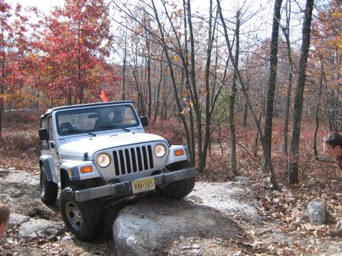 1990 Ford Bronco - A white Jeep Wrangler navigates a rocky trail during autumn, with trees displaying red and orange leaves.