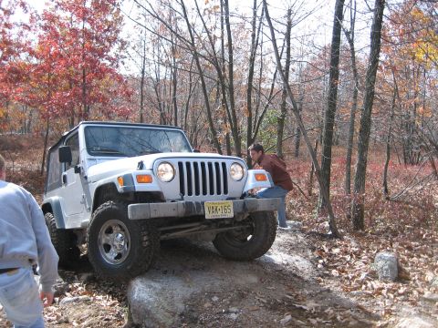 1990 Ford Bronco - A white Jeep Wrangler tackles a challenging off-road course amidst autumn trees.