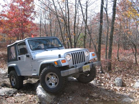 1990 Ford Bronco - Silver Jeep Wrangler TJ navigating a rocky trail with fall foliage in the background.