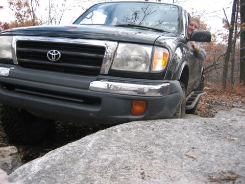 1990 Ford Bronco - A Toyota Tacoma navigates a rocky trail, with its front tire lodged on a large boulder.