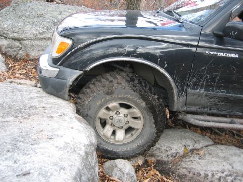 1990 Ford Bronco - A black Toyota Tacoma navigates a rocky trail, its front tire wedged between boulders.