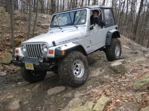1990 Ford Bronco - Silver Jeep Wrangler TJ navigates a rocky off-road trail with a driver visible inside.