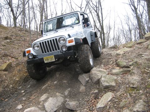 1990 Ford Bronco - A silver Jeep Wrangler navigates a challenging rocky off-road trail.