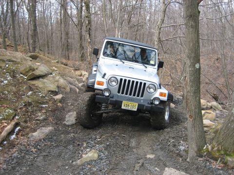 1990 Ford Bronco - This Jeep Wrangler is shown tackling a challenging, rocky trail in a wooded area.