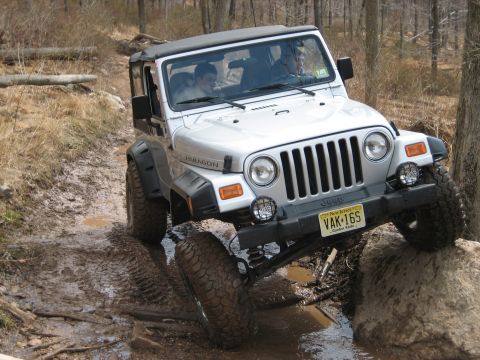 1990 Ford Bronco - This Jeep Wrangler TJ navigates a challenging off-road course with muddy terrain and large rocks.