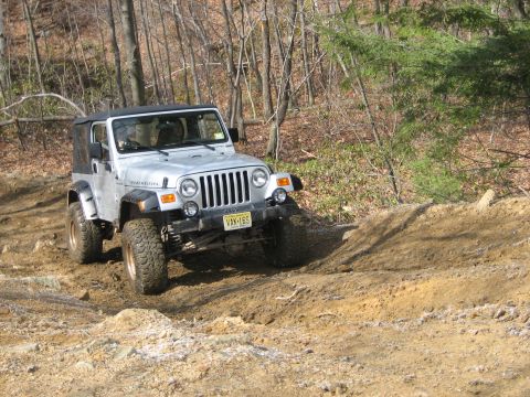 1990 Ford Bronco - A Jeep Wrangler TJ navigates a challenging off-road course with steep inclines and loose dirt.