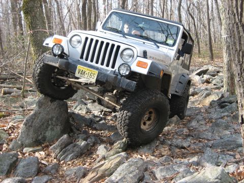 1990 Ford Bronco - A silver Jeep Wrangler tackles a challenging rocky off-road course.