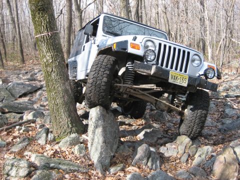 1990 Ford Bronco - White Jeep Wrangler TJ navigating a difficult rocky trail.
