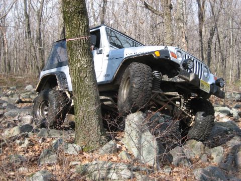 1990 Ford Bronco - This Jeep Wrangler TJ is shown off-roading over large rocks in a wooded area.