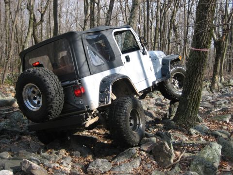 1990 Ford Bronco - A white Jeep Wrangler navigates a challenging off-road course through a wooded area.