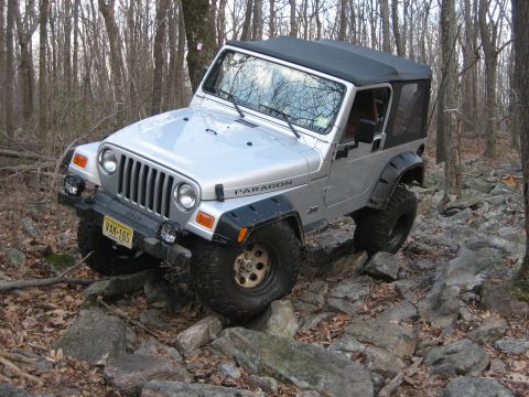 1990 Ford Bronco - Silver Jeep Wrangler TJ shown off-roading through a rocky forest trail.
