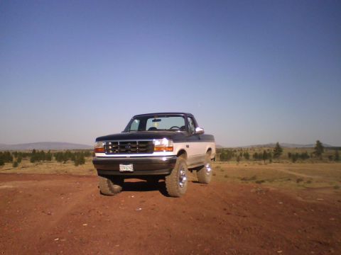1993 Ford Bronco - This two-tone pickup truck is parked on a dirt road with a dry, hilly landscape in the background.