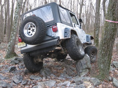 1990 Ford Bronco - A Jeep Wrangler navigates a rocky trail in a wooded area.