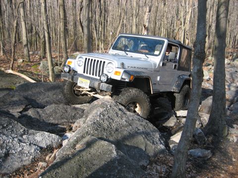 1990 Ford Bronco - This Jeep Wrangler TJ is shown off-roading over large rocks in a forest.