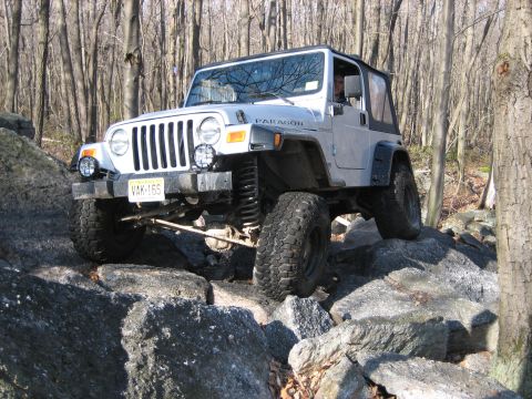 1990 Ford Bronco - This Jeep Wrangler TJ is shown off-roading over large rocks in a wooded area.