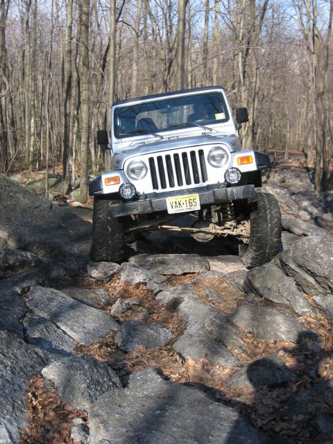 1990 Ford Bronco - A Jeep Wrangler navigates a challenging rocky path through a wooded area.