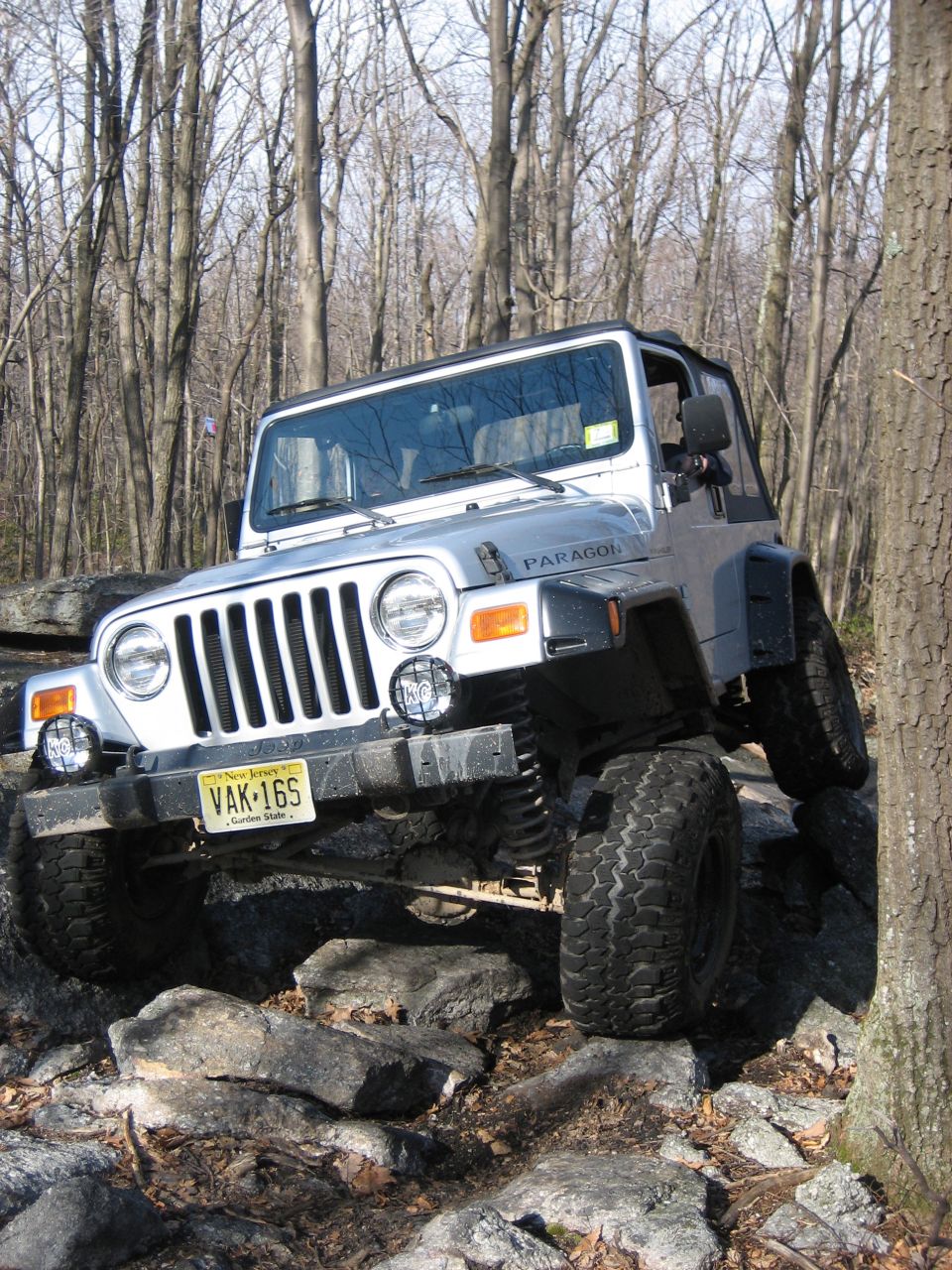 Silver Jeep Wrangler TJ on rocks, front 3/4 view. Yellow New Jersey license plate VAK-16S