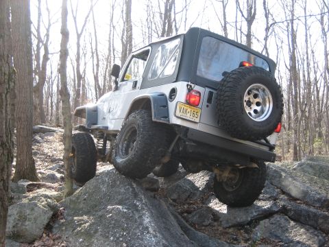 1990 Ford Bronco - A white Jeep Wrangler TJ navigates a rocky trail, demonstrating its off-road capabilities.