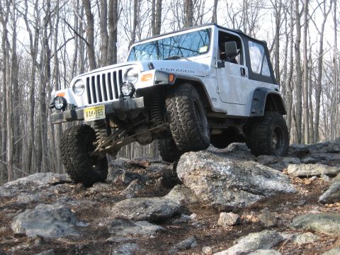 1990 Ford Bronco - Silver Jeep Wrangler TJ navigating a rocky trail in a wooded area.