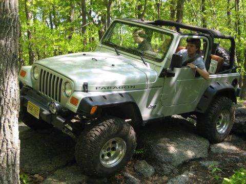 1990 Ford Bronco - A silver Jeep Wrangler navigates a rocky trail in a wooded area.