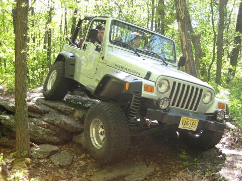 1990 Ford Bronco - A silver Jeep Wrangler navigates a rocky trail, demonstrating its off-road capabilities.