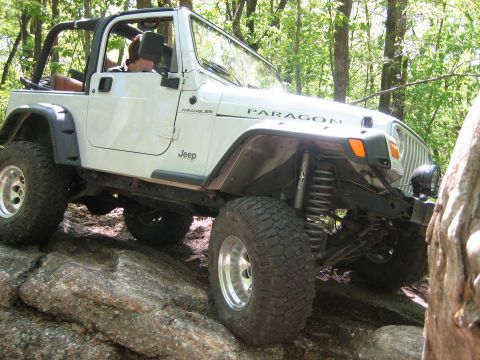 1990 Ford Bronco - This white Jeep Wrangler navigates a rocky trail through a wooded area.