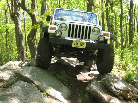 1990 Ford Bronco - White Jeep Wrangler TJ navigating a rocky off-road trail.