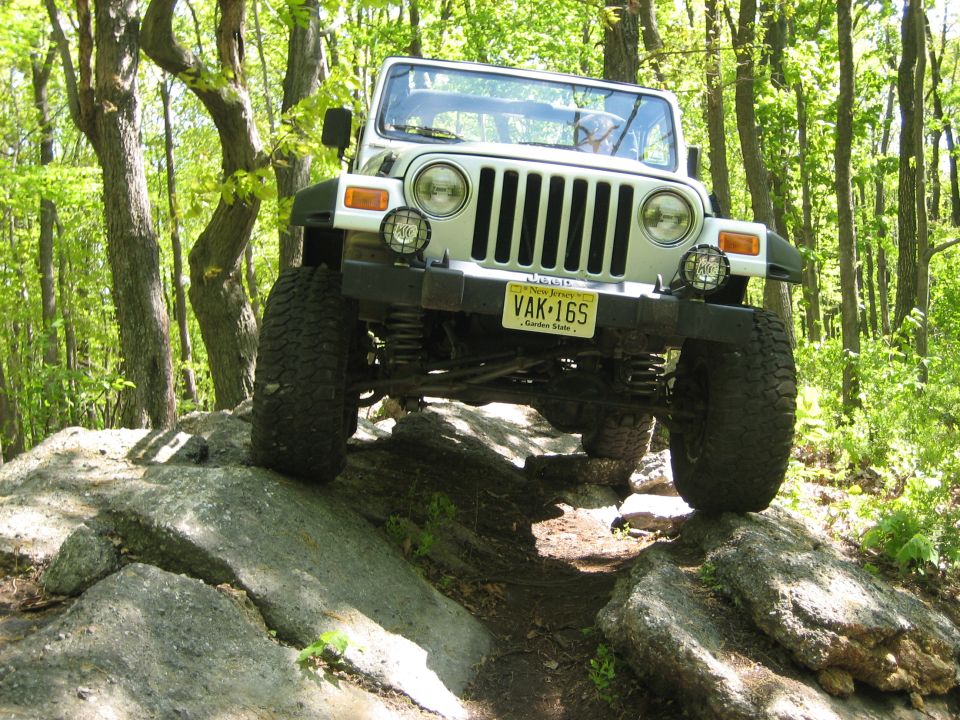White Jeep Wrangler TJ climbing over rocks on a trail. License plate VAK-16S
