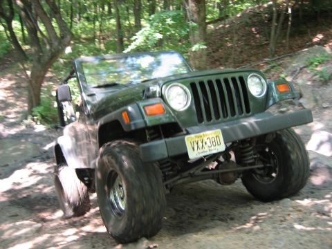 1990 Ford Bronco - This Jeep Wrangler is navigating a rocky and muddy off-road path through a wooded area.