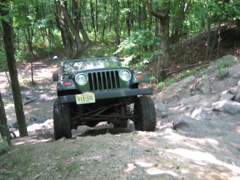 1990 Ford Bronco - A green Jeep Wrangler navigates a muddy and rocky off-road trail.