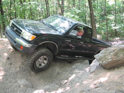 1990 Ford Bronco - A black Toyota Tacoma navigates a challenging rocky trail, demonstrating its off-road capabilities.