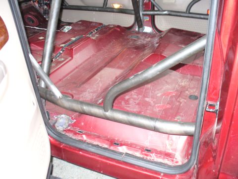 1978 Ford Bronco - Interior view of a red vehicle a custom roll cage and bare metal floor.