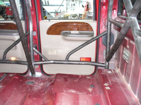 1978 Ford Bronco - The interior of a red truck shows a custom roll cage and a wood-grain door panel.