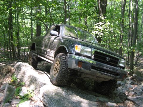 1990 Ford Bronco - This Toyota pickup truck is shown off-roading on a rocky trail through a wooded area.