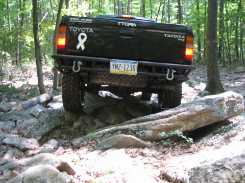 1990 Ford Bronco - This Toyota Tacoma is tackling a challenging off-road trail with large rocks and trees.