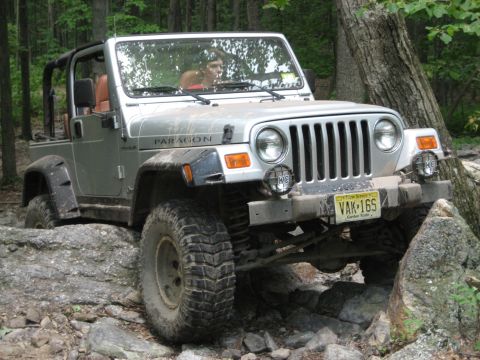 1990 Ford Bronco - A silver Jeep Wrangler tackles a challenging rocky trail, demonstrating its off-road capabilities.
