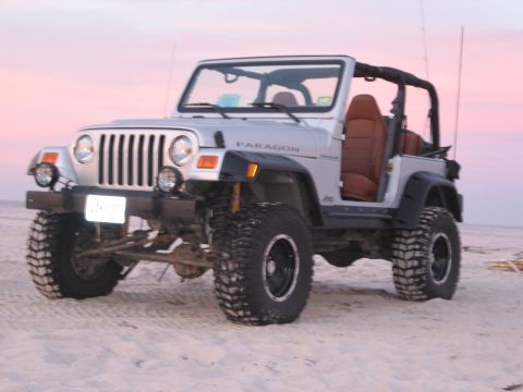 1990 Ford Bronco - Silver Jeep Wrangler with aftermarket modifications parked on a sandy beach at sunset.