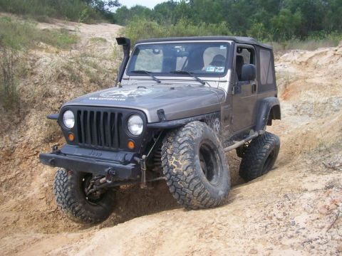 2004 Jeep Wrangler - A gray Jeep Wrangler navigates a steep, sandy incline with large off-road tires.
