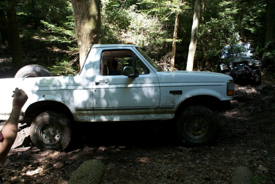 White Ford pickup truck off-road on a muddy wooded trail