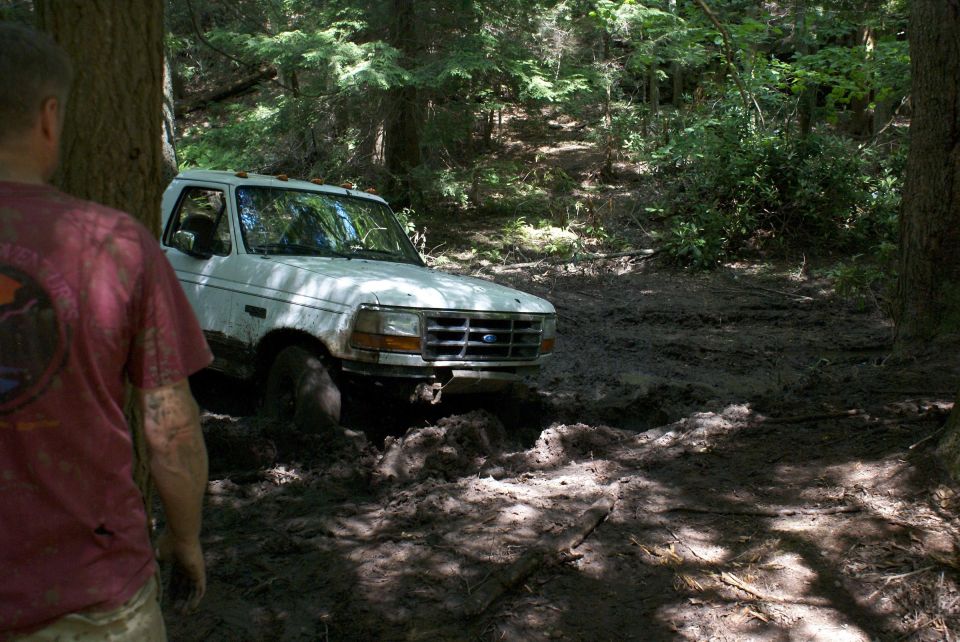 White Ford truck buried in mud with a muddy man watching