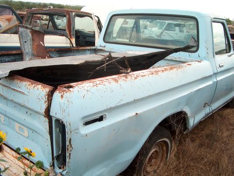 1979 Ford Bronco - Junkyard scene with a damaged light blue pickup truck. Other vehicles are visible in the background.