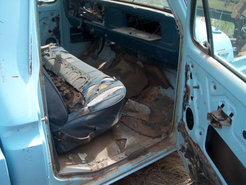 1979 Ford Bronco - The interior of a light blue pickup truck shows a torn seat with engine parts and a rusty floor.